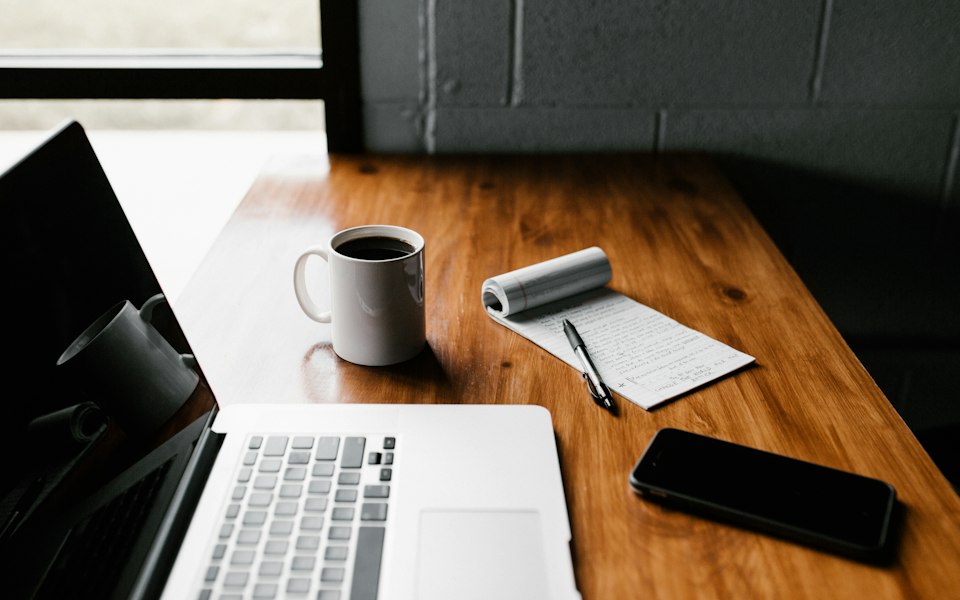 Laptop, Notizblock und Kaffeetasse auf einem Holztisch